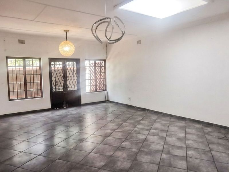 Spacious, empty living area featuring tiled flooring, security gates on windows and doors, and an installed air conditioning unit.