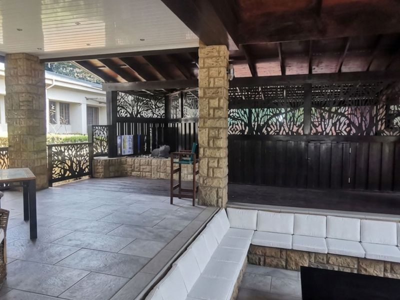 A spacious covered patio featuring stone pillars, timber ceiling, tiled flooring, and decorative privacy screens, offering a comfortable outdoor entertainment area.