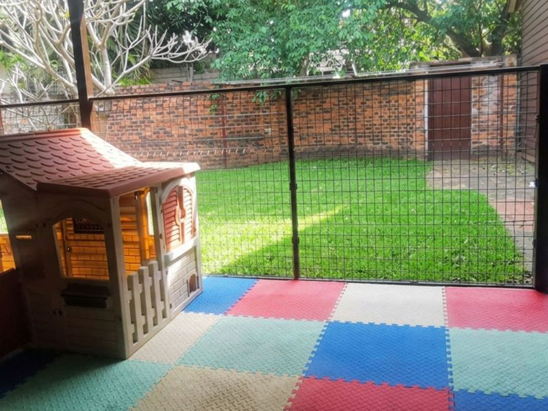 A covered outdoor patio area featuring paved flooring and secure wire mesh fencing, overlooking a private rear garden with a brick boundary wall.