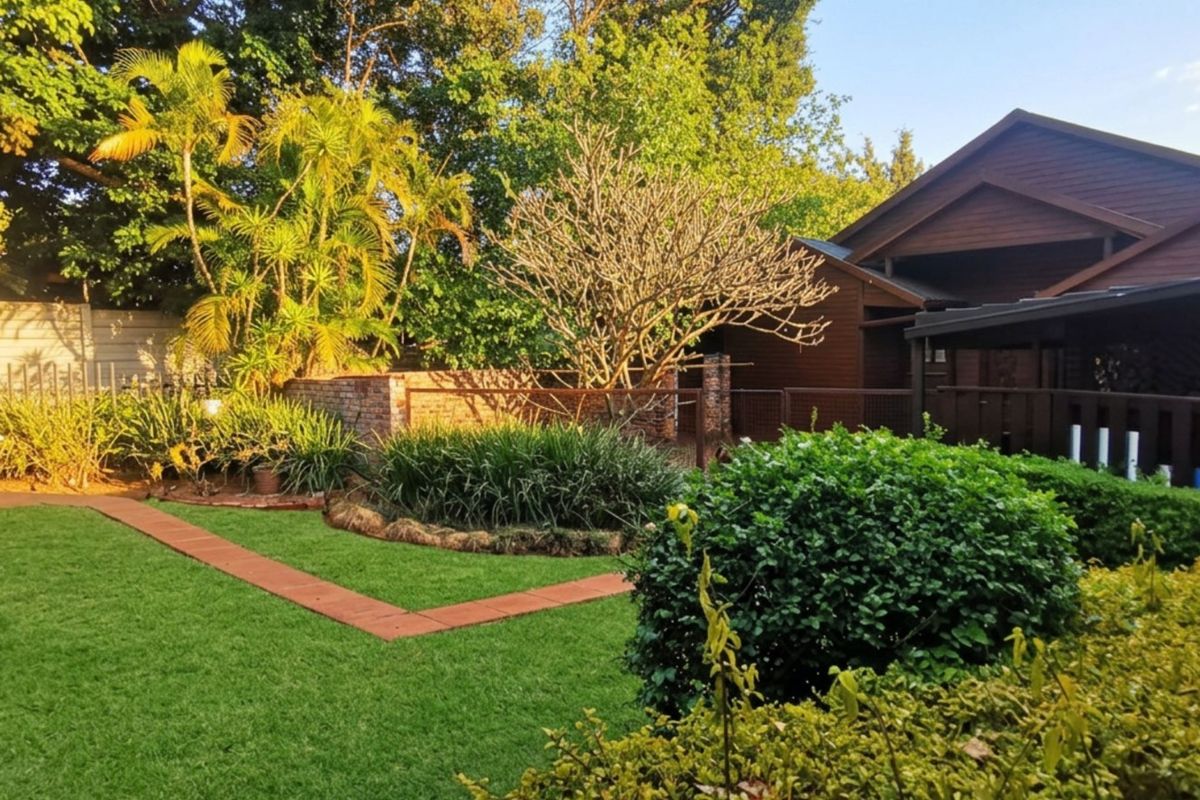 A well-maintained rear garden featuring a lush lawn, paved pathways, established landscaping, and a covered patio area adjacent to the timber-clad house.