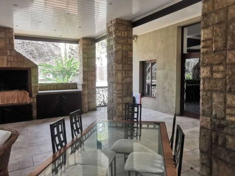 Spacious covered patio featuring a built-in stone braai, stone-clad support pillars, and tiled flooring, ideal for outdoor entertaining.