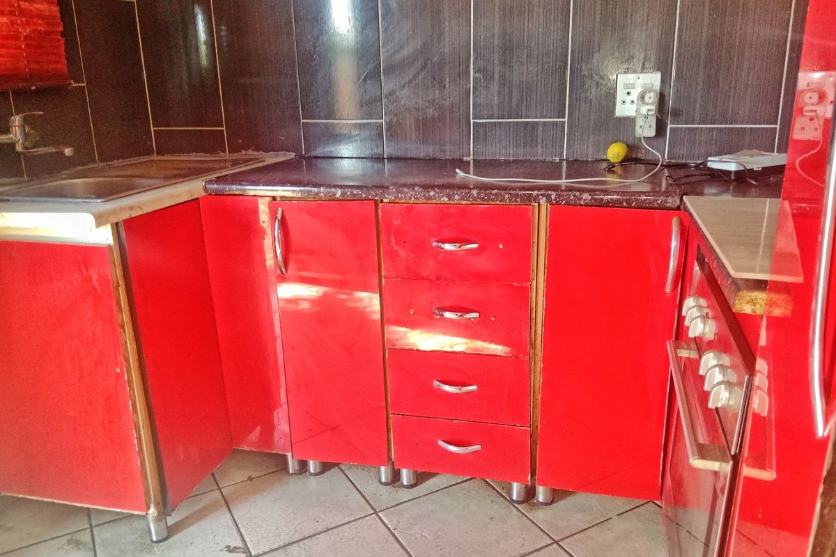 A kitchen area featuring red cabinetry, a dark tiled backsplash, and a built-in oven, requiring cosmetic updates to improve the overall aesthetic.