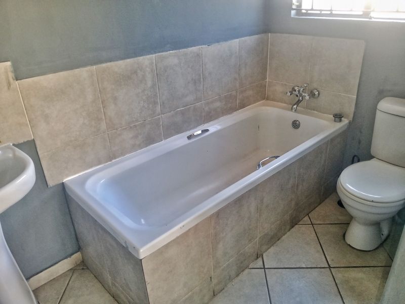 A functional bathroom featuring a standard bathtub, pedestal basin, and toilet with neutral wall and floor tiling.