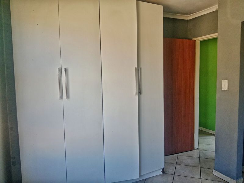 A bedroom interior featuring built-in cupboards and tiled flooring, leading to an adjacent room with a green accent wall.