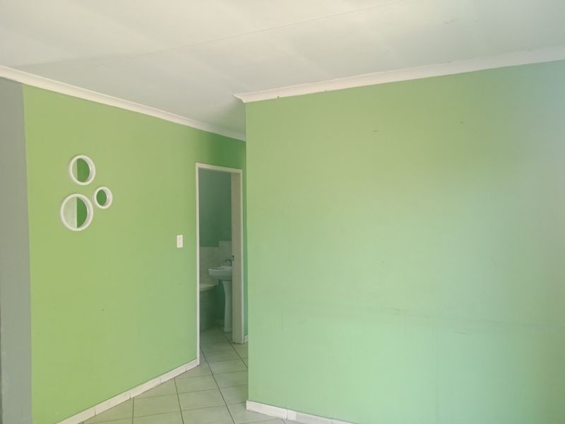 A vacant hallway featuring light green walls, tiled flooring, and a view into an adjacent bathroom with a pedestal sink.