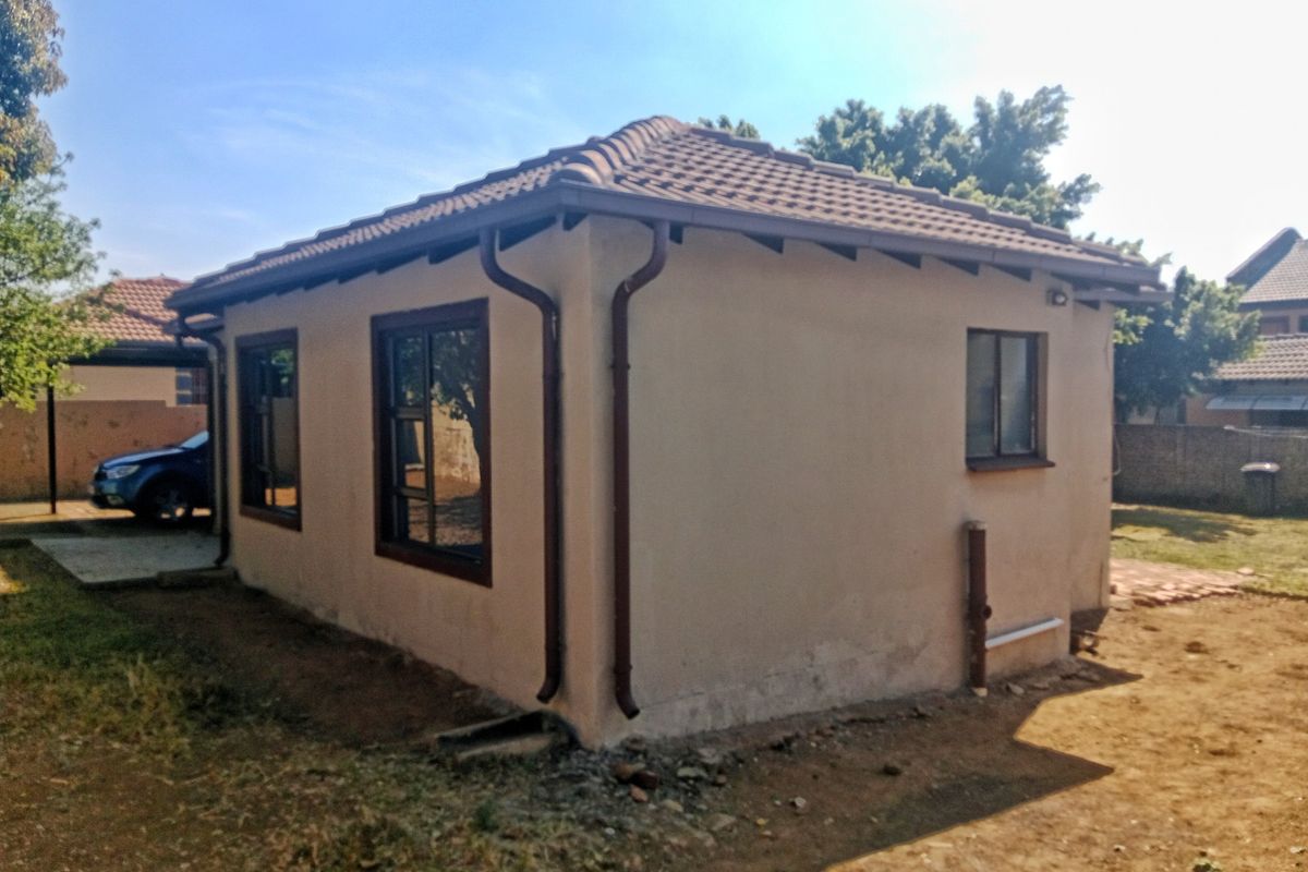 Rear view of a single-story residential building featuring a tiled roof, brown gutters, and aluminium window frames.