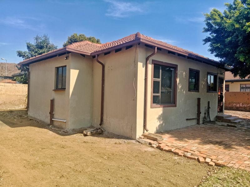 Rear view of the property showing the exterior facade, tiled roof, gutter system, and brick paved patio area.