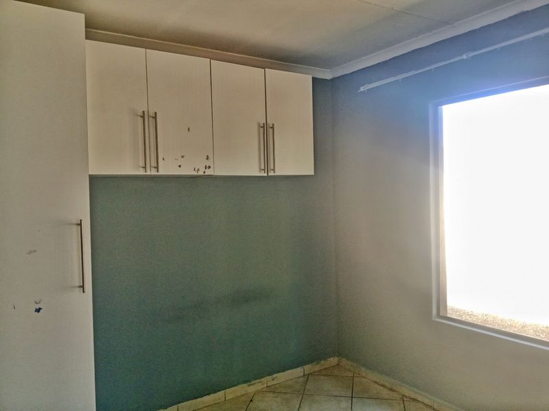 An empty bedroom featuring built-in cupboards, tiled flooring, and a window, requiring minor cosmetic updates to refresh the space.