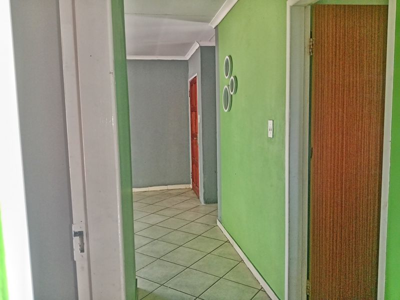 A vacant hallway featuring tiled flooring and painted walls, providing access to multiple rooms within the property.
