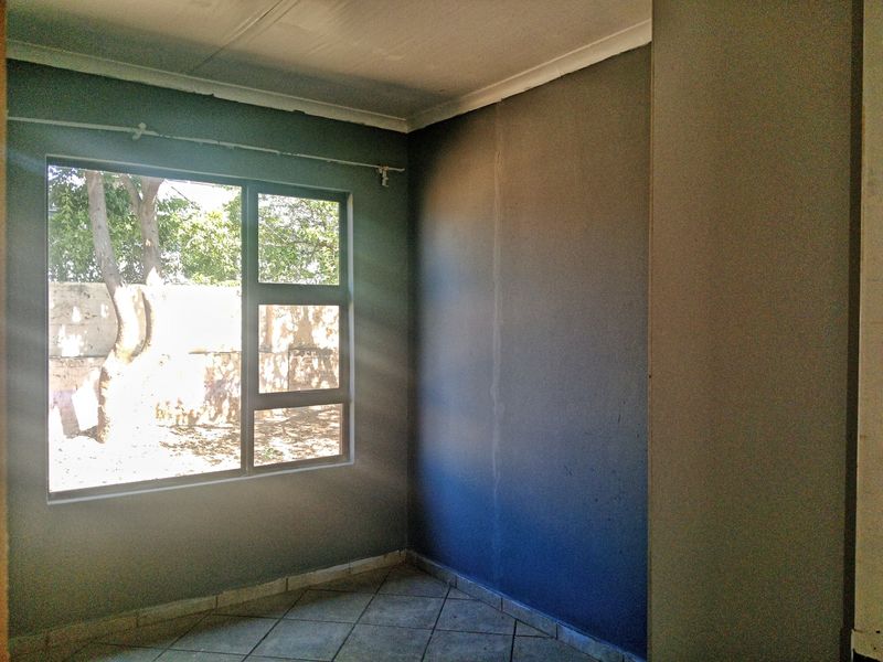 An empty bedroom featuring tiled flooring and a large window, requiring cosmetic updates to the wall finishes.