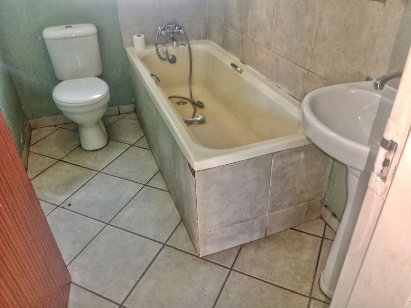 A functional bathroom featuring a pedestal basin, toilet, and a bathtub with a handheld shower mixer, requiring cosmetic updates to modernize the space.