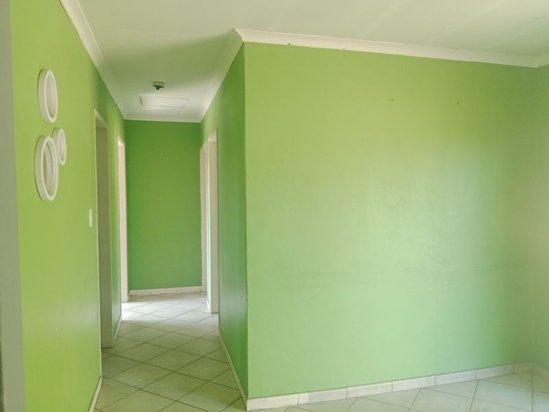 A vacant hallway featuring tiled flooring and bright green painted walls, providing access to multiple rooms within the home.