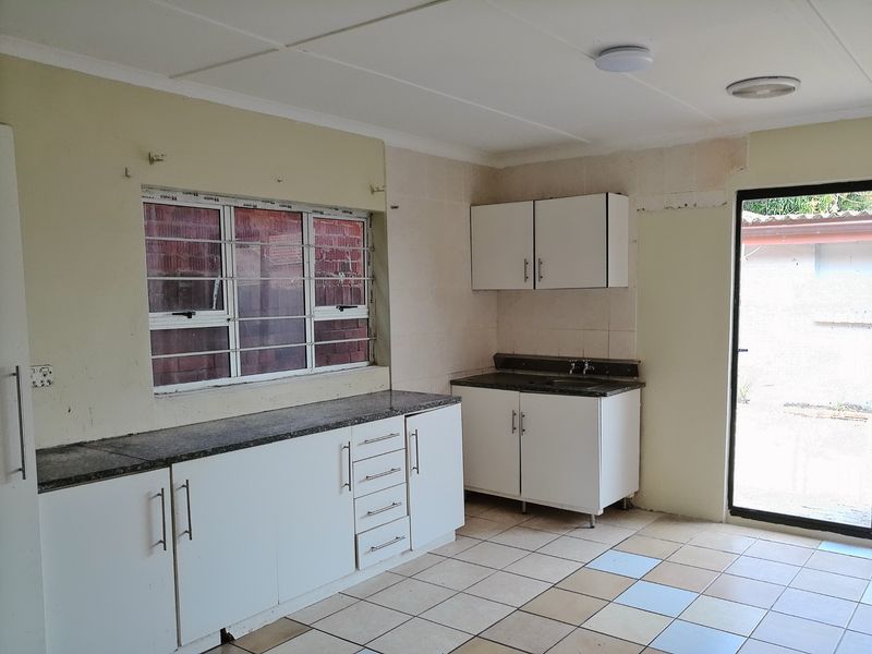 A functional kitchen space featuring granite countertops, white cabinetry, and tiled flooring, currently empty and ready for renovation or modernization.