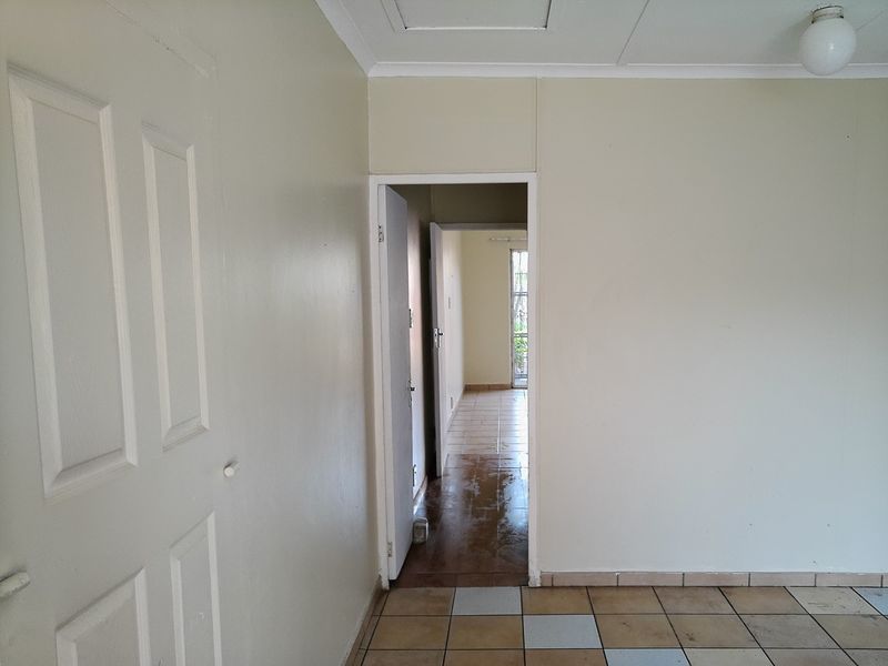 A vacant hallway featuring tiled flooring and a ceiling access hatch, providing a clear view through to an adjacent room.