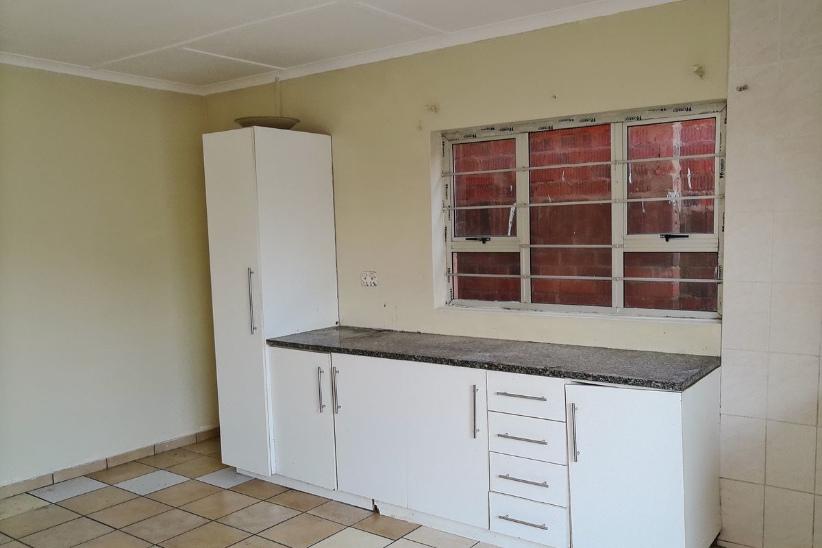 A functional kitchen area featuring white built-in cabinetry, granite countertops, and tiled flooring, ready for a modern update.