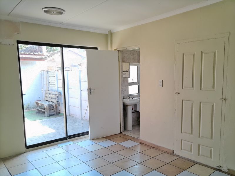 An empty living area featuring tiled flooring, a sliding glass door leading to a patio, and direct access to an adjacent bathroom.