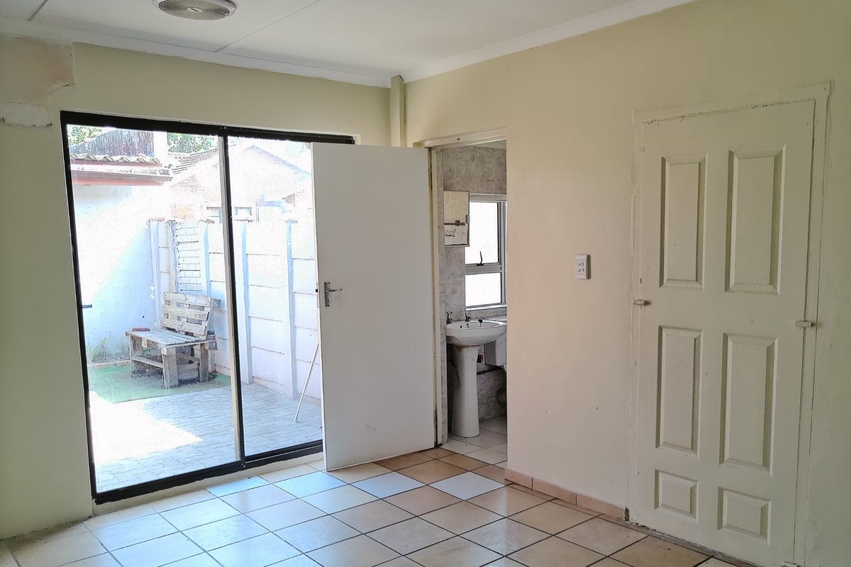 An empty living area featuring tiled flooring, a sliding glass door leading to a patio, and direct access to an adjacent bathroom.