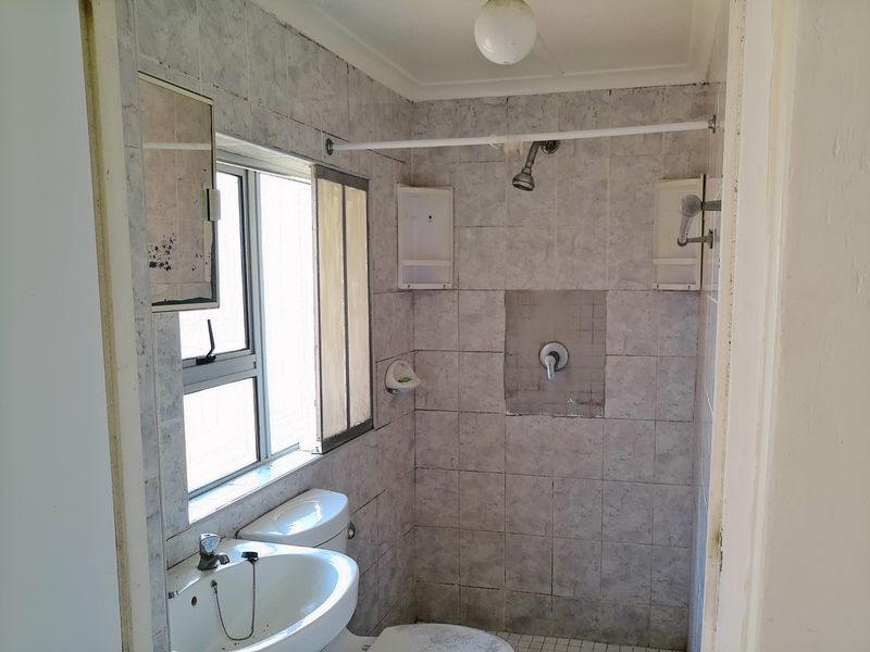A dated bathroom featuring a shower, basin, and toilet with original tiled finishes, requiring modernization and cosmetic updates.