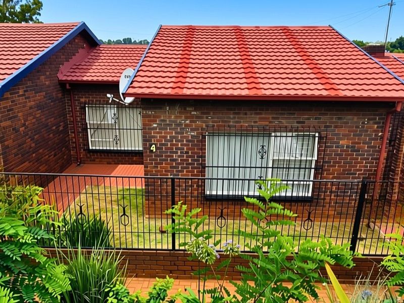 Front view of a face brick house featuring a tiled roof, security bars on windows, and a small fenced garden area.