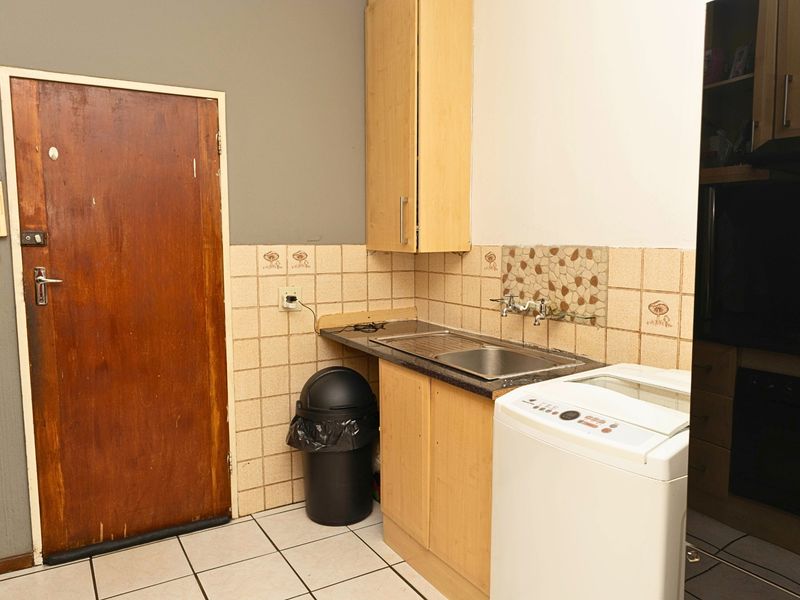 A functional laundry area featuring built-in cabinetry, a stainless steel sink, tiled backsplash, and tiled flooring.