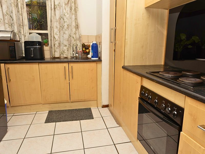 A functional kitchen featuring light wood cabinetry, dark laminate countertops, tiled flooring, and a built-in oven with an electric hob.