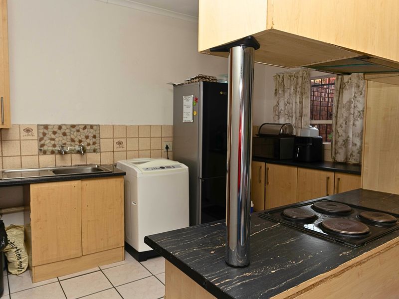 Functional kitchen featuring laminate cabinetry, dark countertops, an integrated electric hob, and tiled backsplash with a practical layout.