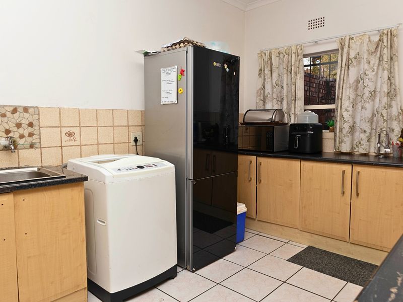 Functional kitchen featuring light wood cabinetry, dark laminate countertops, tiled backsplash, and ceramic floor tiles with space for laundry appliances.