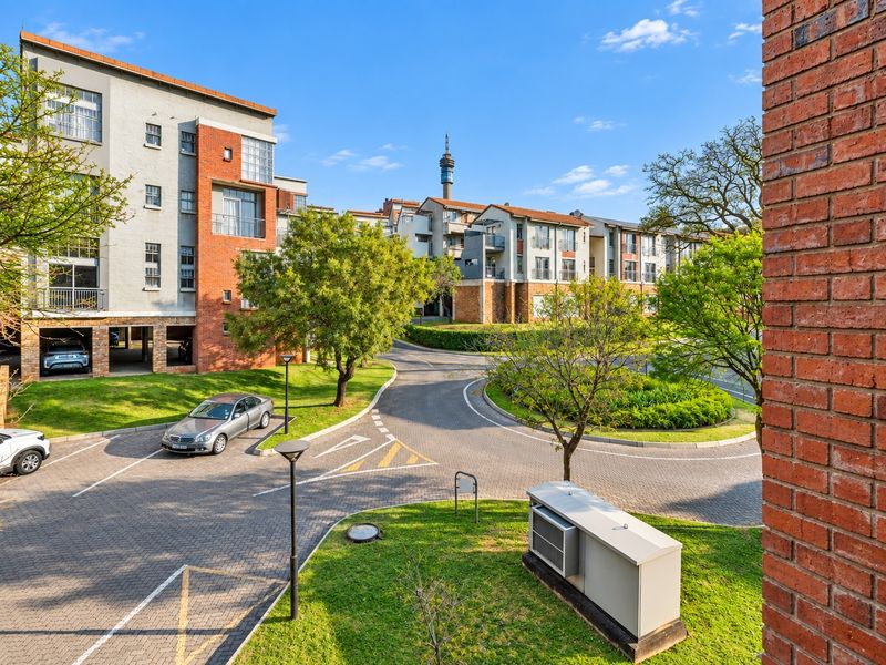 A view of the apartment complex grounds featuring paved driveways, landscaped gardens, and multi-story residential buildings with brick and plaster facades.