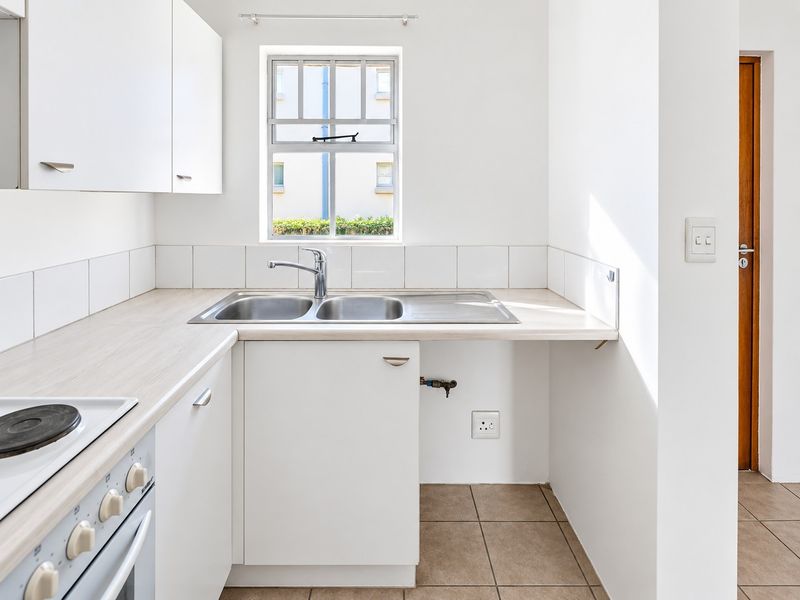 A clean, functional kitchen featuring white cabinetry, laminate countertops, a stainless steel double sink, and an integrated electric stove with tiled flooring.
