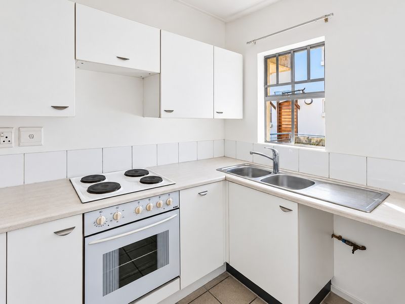 A functional kitchen featuring white cabinetry, laminate countertops, a built-in oven with electric hob, and a double stainless steel sink.