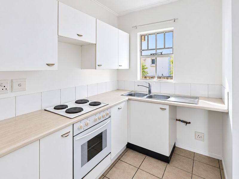 A clean, functional kitchen featuring white cabinetry, a built-in oven with electric hob, double sink, and tiled flooring.