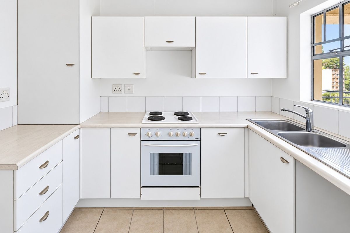 A clean, functional kitchen featuring white cabinetry, laminate countertops, a built-in oven with electric hob, and a double stainless steel sink.