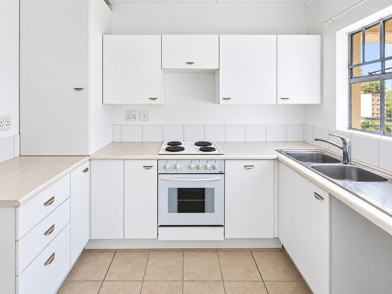 A clean, functional kitchen featuring white cabinetry, laminate countertops, a built-in oven with electric hob, and a double stainless steel sink.