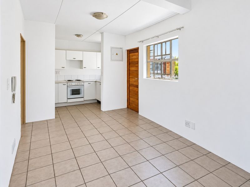 An open-plan living and kitchen area featuring neutral tiled flooring, white cabinetry, and an integrated electric stove, offering a clean and functional layout.