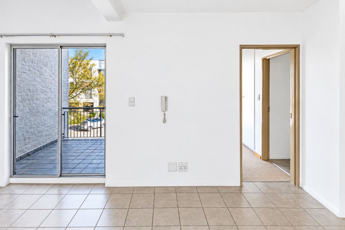 An empty living area featuring tiled flooring, an intercom system, and a sliding glass door providing access to a balcony.
