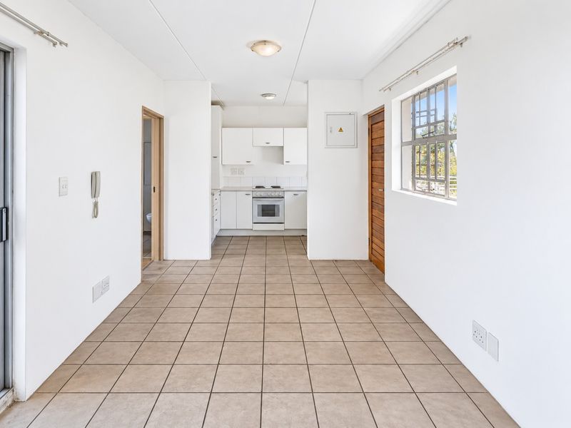 An open-plan living and kitchen area featuring tiled flooring, white cabinetry, and a functional stove, offering a clean, blank canvas for personalization.
