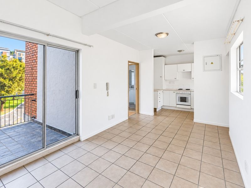 Open-plan living area featuring tiled floors, a compact kitchen with built-in appliances, and direct access to a private balcony.