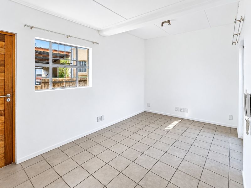 A bright, empty bedroom featuring neutral tiled flooring, a steel-framed window, and a solid timber door, providing a clean canvas for personalization.