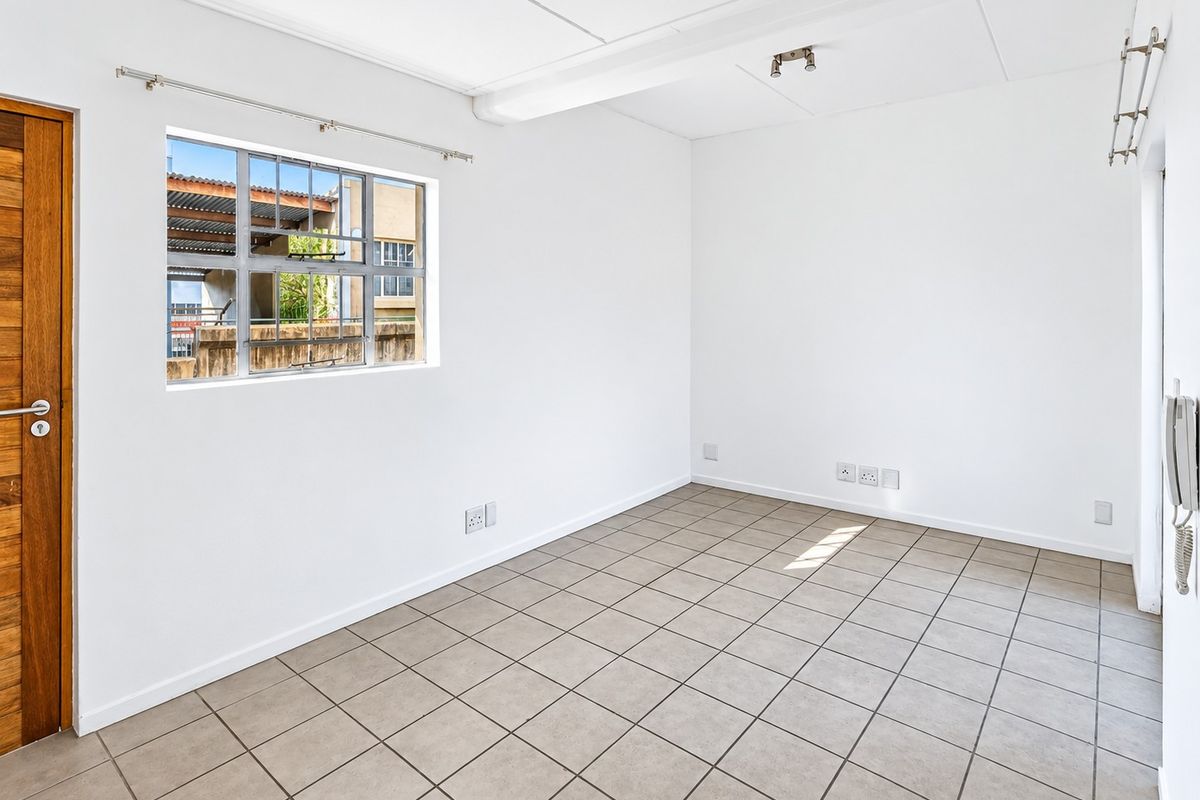 A bright, empty bedroom featuring neutral tiled flooring, a steel-framed window, and a solid timber door, providing a clean canvas for personalization.