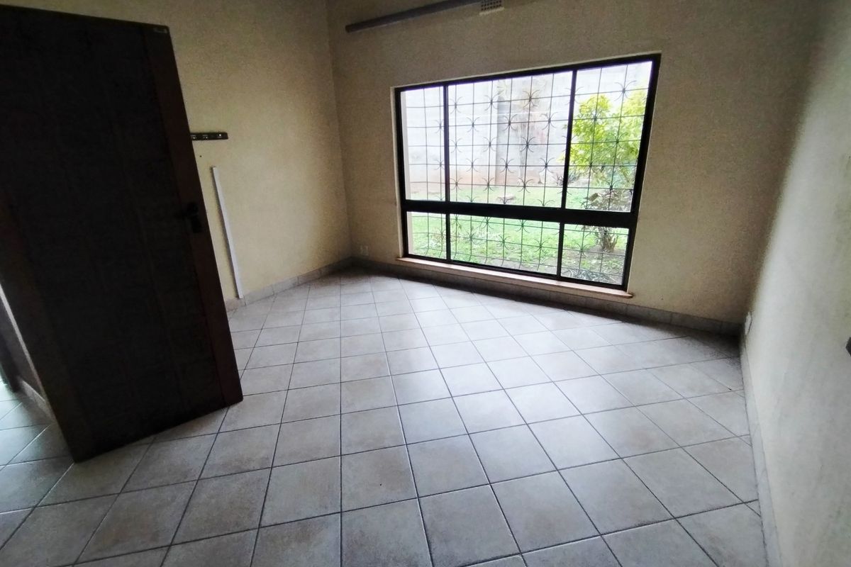 A vacant bedroom featuring neutral tiled flooring, a large window with security bars, and a standard internal door, offering a clean, blank canvas.