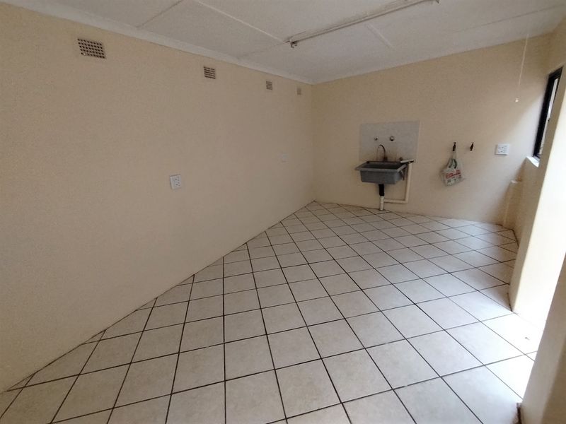 A functional, empty laundry room featuring tiled flooring and a wall-mounted utility sink with plumbing connections.