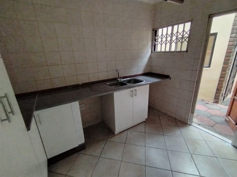 A functional scullery area featuring built-in cabinetry, a stainless steel sink, tiled splashbacks, and direct access to an outdoor area.