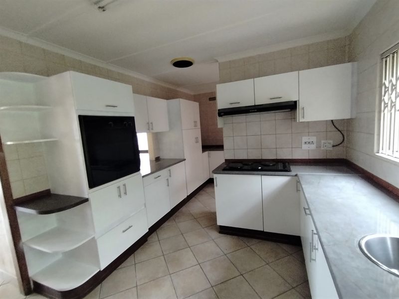A functional kitchen featuring white built-in cabinetry, laminate countertops, a built-in oven, hob, extractor fan, and tiled finishes throughout.