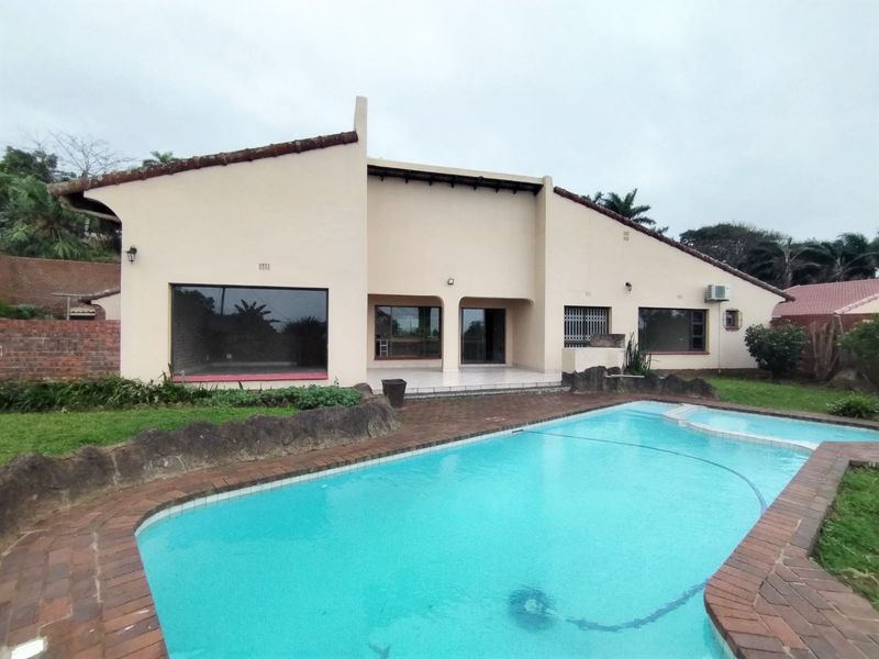 Rear exterior view of the house featuring a swimming pool with brick coping, a tiled patio area, and established garden landscaping.