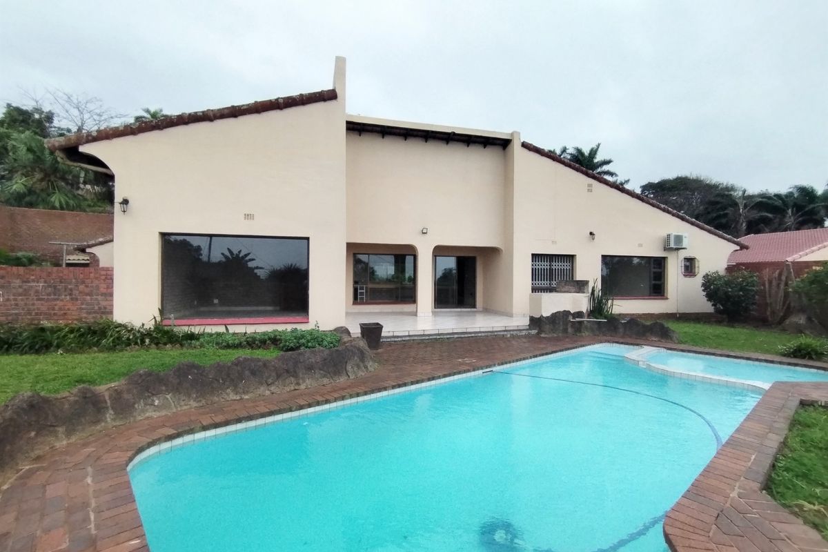 Rear exterior view of the house featuring a swimming pool with brick coping, a tiled patio area, and established garden landscaping.