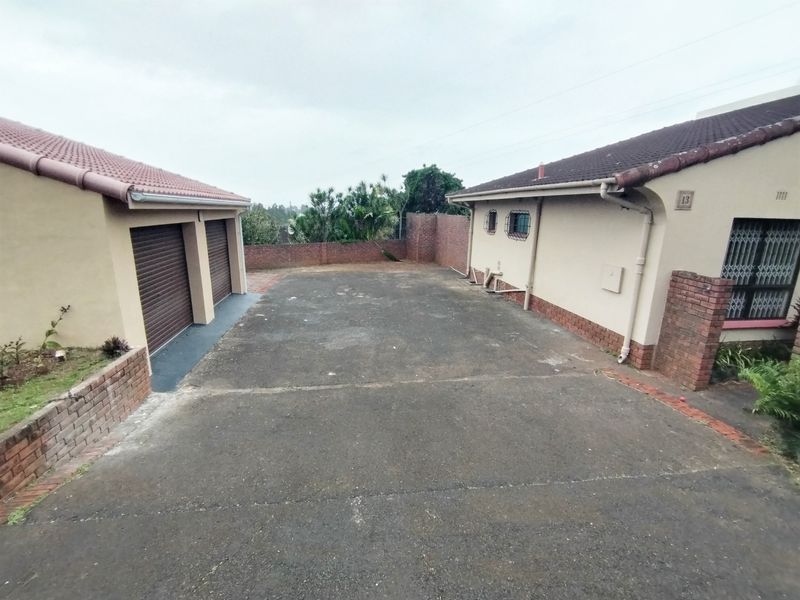 Front exterior view showing a concrete driveway, double garage, and brick boundary wall, providing access to the main residence.