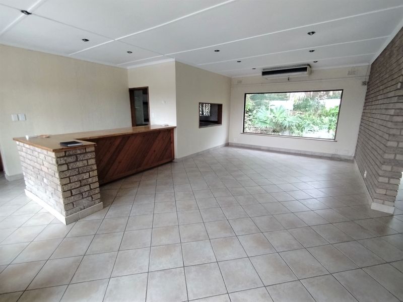 Spacious living area featuring a built-in bar, brick accent wall, tiled flooring, and large window with garden views.