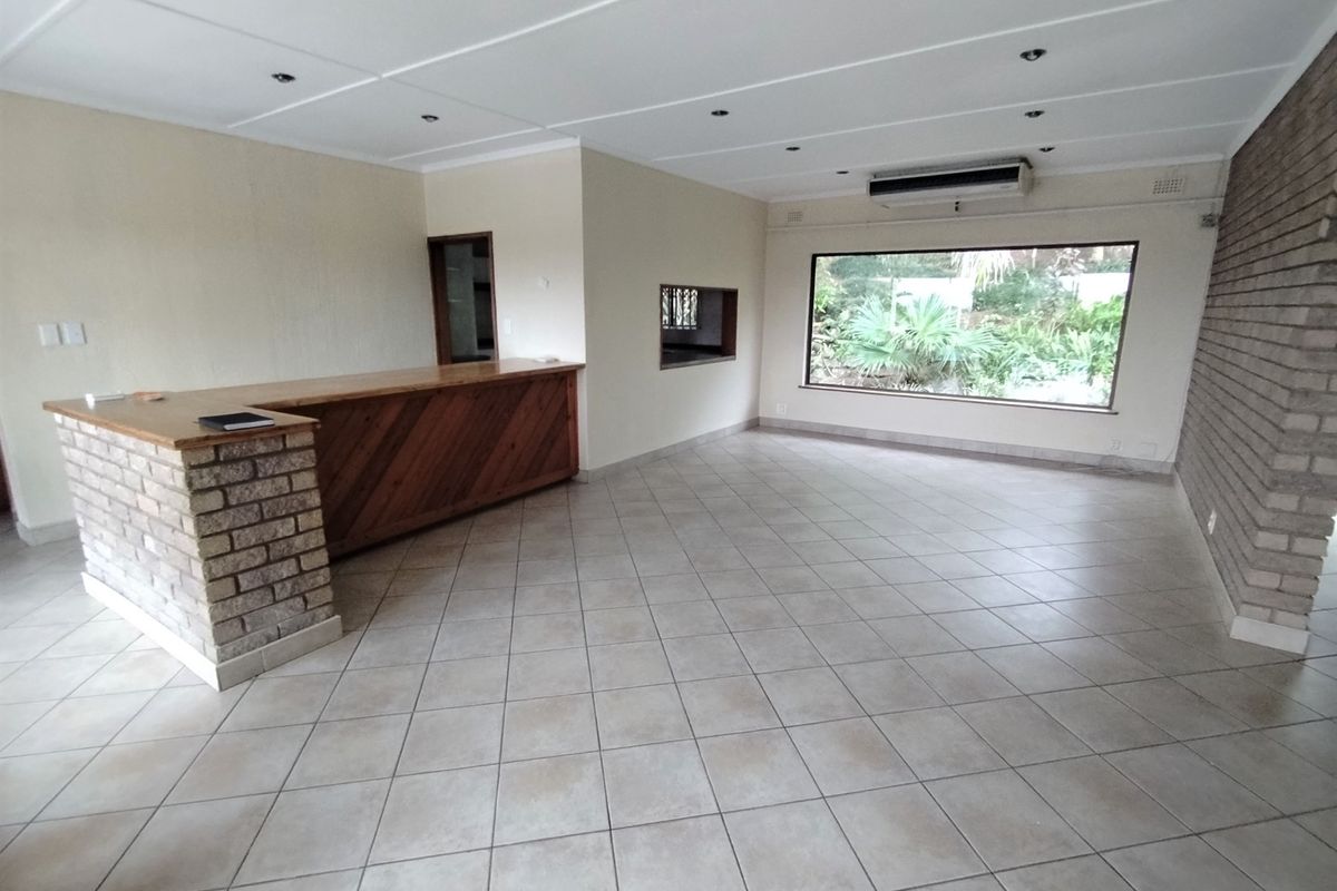 Spacious living area featuring a built-in bar, brick accent wall, tiled flooring, and large window with garden views.