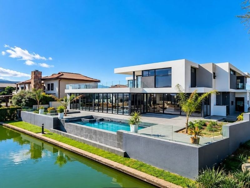Modern waterfront residence featuring a sleek architectural design, expansive glass sliding doors, a private swimming pool, and a spacious patio overlooking the canal.