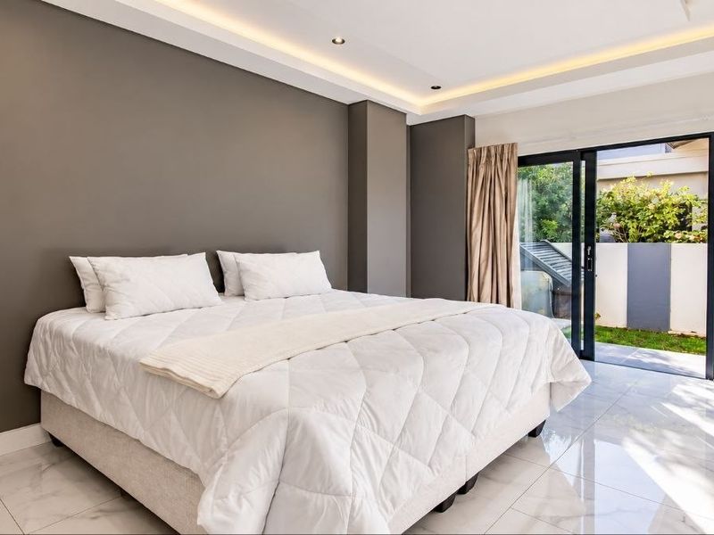 Modern bedroom featuring sleek tiled flooring, recessed ceiling lighting, and large sliding glass doors providing direct access to the garden area.